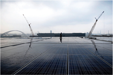 A man walks near solar energy panels on the top floor of the Theme Pavilion at the Shanghai Expo Site in Shanghai, China. The 30,000 square meters of solar energy panels sit on the top floor of the Theme Pavilion, which could generate 2.5 megawatts of electricity per hour on sunny days. Source: Photo by Liu Jianfeng/ChinaFotoPress.